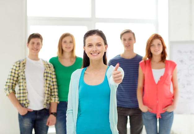 koncepcja edukacji i szkoły - grupa uśmiechniętych uczniów z nastolatką z przodu pokazującą kciuk w górę