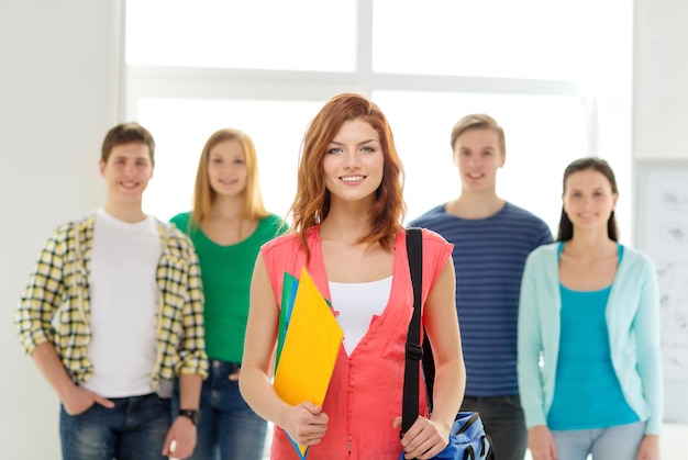 koncepcja edukacji i szkoły - grupa uśmiechniętych uczniów z nastolatką z przodu z torbą i folderami