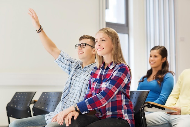 koncepcja edukacji, liceum, pracy zespołowej i ludzi - grupa uśmiechniętych studentów podnosi rękę w sali wykładowej
