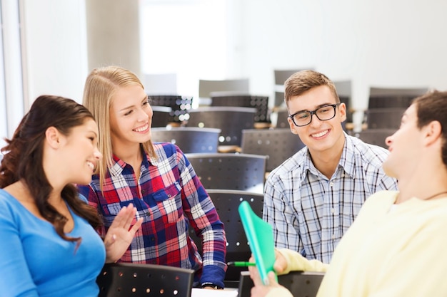 Zdjęcie koncepcja edukacji, liceum, pracy zespołowej i ludzi - grupa uśmiechniętych studentów z notatnikiem siedząca w sali wykładowej i rozmawiająca