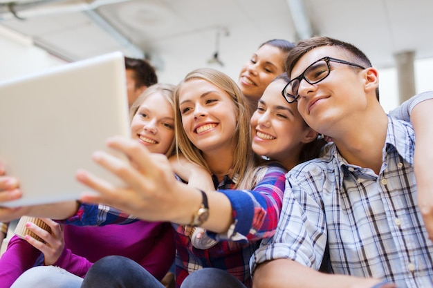 koncepcja edukacji, liceum, technologii i ludzi - grupa uśmiechniętych uczniów z komputerem typu tablet PC, robiąca zdjęcia lub filmy w pomieszczeniu