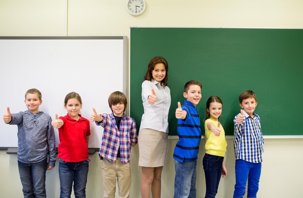 koncepcja edukacji, podstaw, gestów i ludzi - grupa dzieci w wieku szkolnym i nauczyciel pokazujący kciuk w klasie