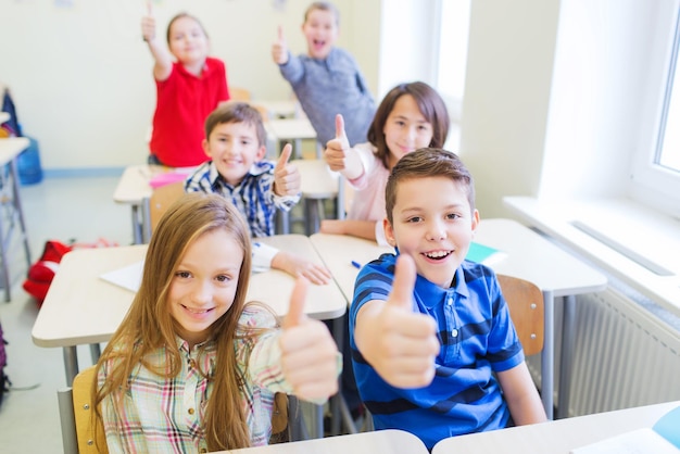 Zdjęcie koncepcja edukacji, szkoły podstawowej, nauki, gestów i ludzi - grupa dzieci w wieku szkolnym siedząca w klasie i pokazująca kciuk w górę
