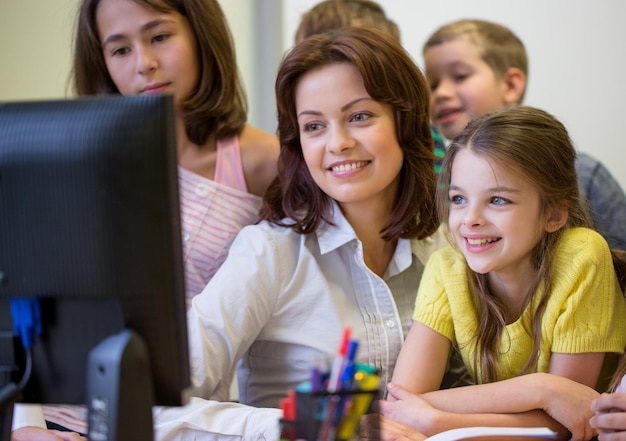 koncepcja edukacji, szkoły podstawowej, nauki, technologii i ludzi - grupa dzieci w wieku szkolnym z nauczycielem patrzącym na monitor komputera w klasie