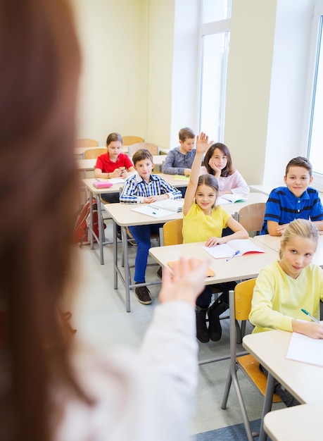 koncepcja edukacji, szkoły podstawowej, uczenia się i ludzi - grupa dzieci w wieku szkolnym z nauczycielem siedzącym w klasie i podnoszącym ręce