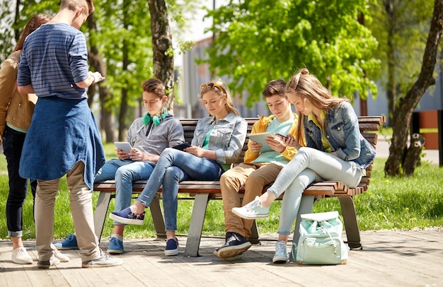 koncepcja edukacji, szkoły średniej i ludzi - grupa szczęśliwych nastoletnich uczniów z komputerami typu tablet PC siedzącymi na ławce na dziedzińcu kampusu