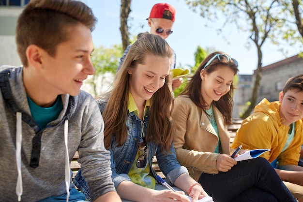 Zdjęcie koncepcja edukacji, szkoły średniej i ludzi - grupa szczęśliwych nastoletnich uczniów z zeszytami uczącymi się na dziedzińcu kampusu