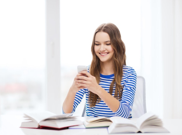 koncepcja edukacji, technologii i domu - szczęśliwa uśmiechnięta studentka ze smartfonem i książkami