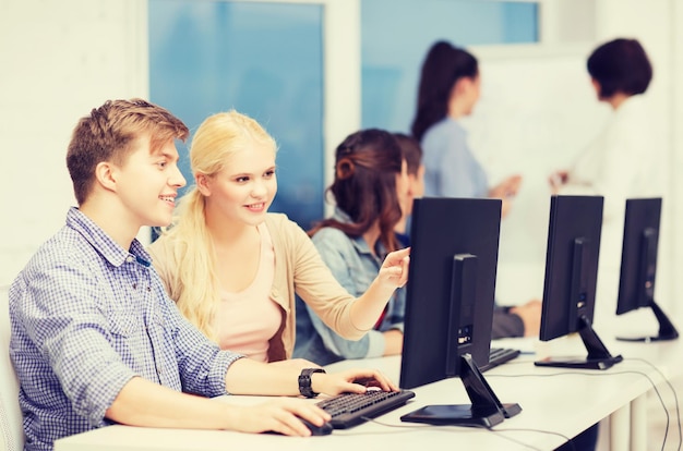 koncepcja edukacji, technologii i internetu - grupa uśmiechniętych uczniów z monitorem komputera patrząca na nauczyciela w szkole