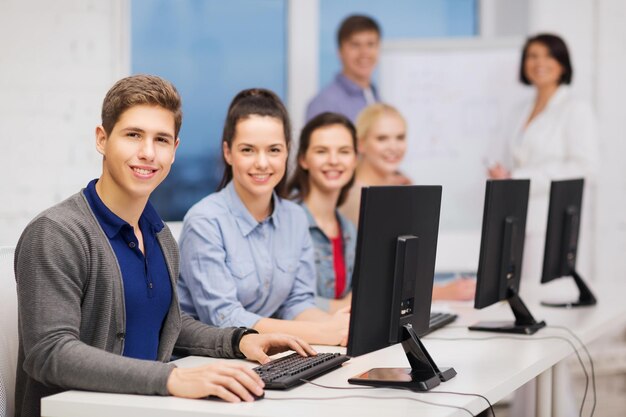 koncepcja edukacji, technologii i internetu - grupa uśmiechniętych uczniów z monitorem komputera w szkole