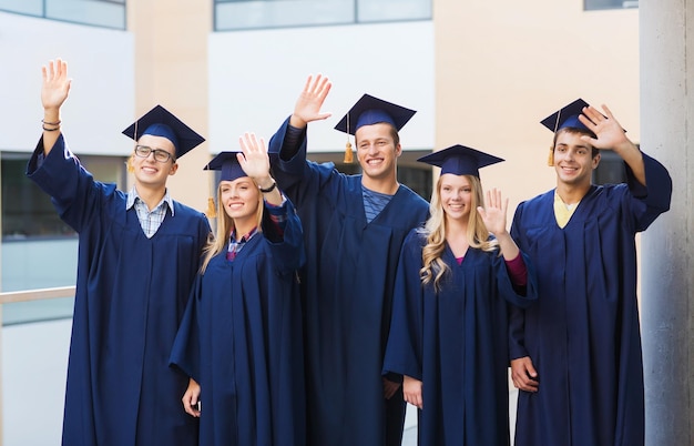 koncepcja edukacji, ukończenia studiów i ludzi - grupa uśmiechniętych studentów w tablicach zapraw i togach machających rękami na zewnątrz