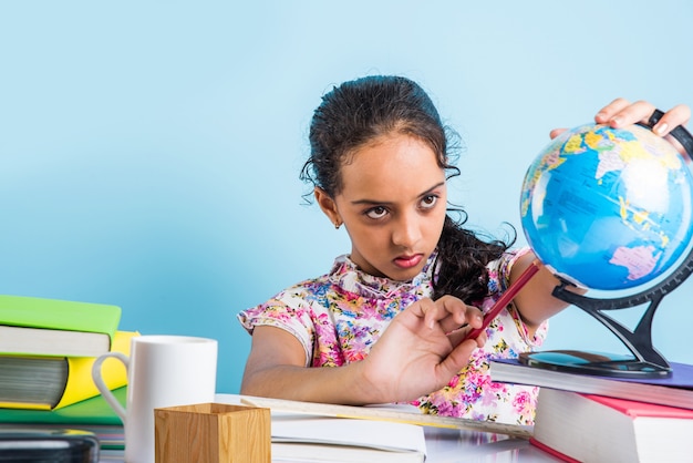 Koncepcja edukacji w domu - Śliczna mała indyjska lub azjatycka dziewczyna ucząca się w domu ze stosem książek, globusem edukacyjnym itp. Selektywne skupienie