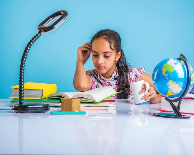 Koncepcja edukacji w domu - Śliczna mała indyjska lub azjatycka dziewczyna ucząca się w domu ze stosem książek, globusem edukacyjnym itp. Selektywne skupienie