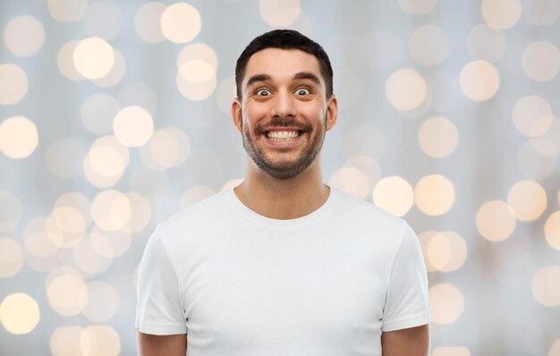 koncepcja ekspresji, emocji i ludzi - mężczyzna z zabawną twarzą na tle świateł świątecznych