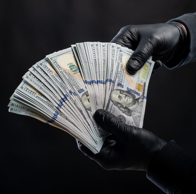 Koncepcja finansów. Mężczyzna w czarnych rękawiczkach trzymający paczkę dolarów na czarnym tle