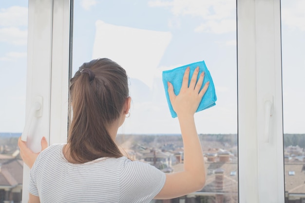 Koncepcja firmy sprzątającej Młoda dziewczyna w rękawiczkach myje okno szmatą