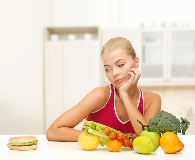 koncepcja fitness, diety i jedzenia - wątpiąca kobieta z owocami i hamburgerem