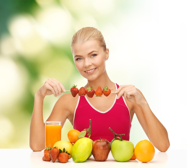 koncepcja fitness, diety i opieki zdrowotnej - uśmiechnięta młoda kobieta z żywnością ekologiczną na stole i truskawkami
