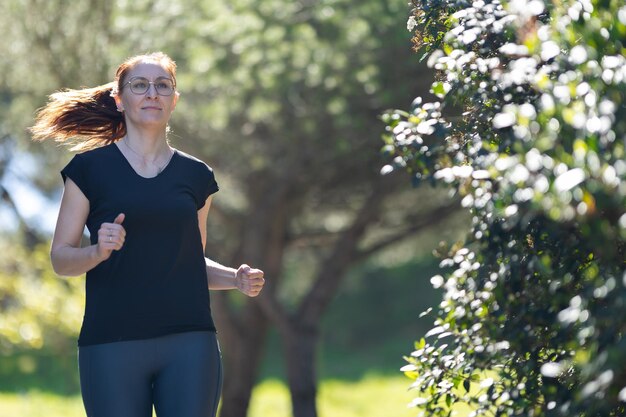 Koncepcja fitness dorosła kobieta w odzieży sportowej biegająca w zielonym parku