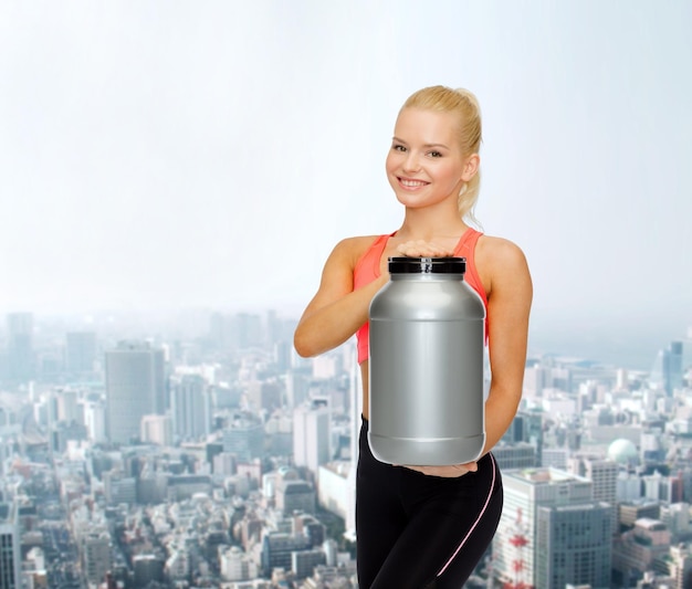 koncepcja fitness i diety - uśmiechnięta wysportowana kobieta ze słoikiem białka