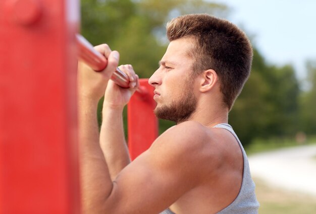 koncepcja fitness, sport, ćwiczenia, trening i styl życia - młody człowiek robi podciąganie na poziomym pasku na zewnątrz