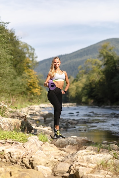 Koncepcja fitness, sport, joga i zdrowy styl życia - młoda kobieta ze szczupłą, zdrową sylwetką stojącą z matą do jogi