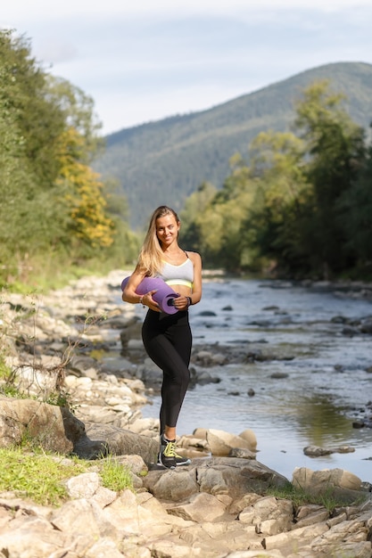 Koncepcja fitness, sport, joga i zdrowy styl życia - młoda kobieta ze szczupłą, zdrową sylwetką stojącą z matą do jogi