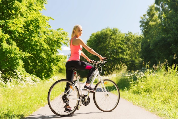 koncepcja fitness, sport, ludzie i zdrowy styl życia - szczęśliwa młoda kobieta jedzie na rowerze na świeżym powietrzu