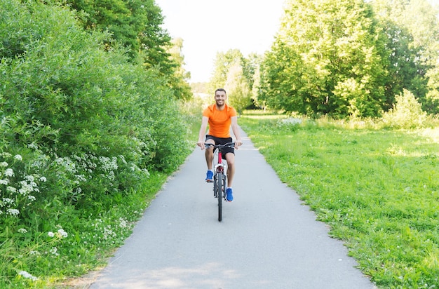 koncepcja fitness, sport, ludzie i zdrowy styl życia - szczęśliwy młody człowiek jedzie na rowerze na zewnątrz