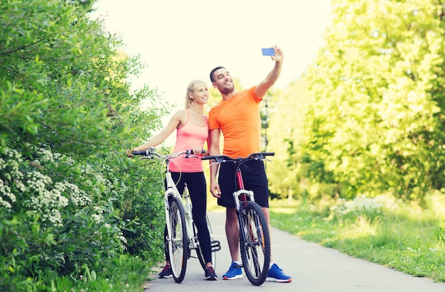 koncepcja fitness, sport, ludzie, technologia i zdrowy styl życia - szczęśliwa para z rowerem biorąca selfie przez smartfon na zewnątrz