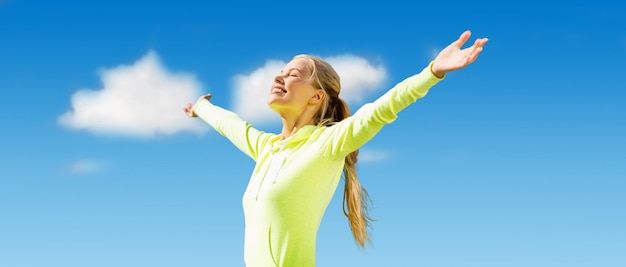 koncepcja fitness, sport, osiągnięcia, ludzie i emocje - szczęśliwa sportowa kobieta ciesząca się słońcem i wolnością na tle błękitnego nieba i chmur