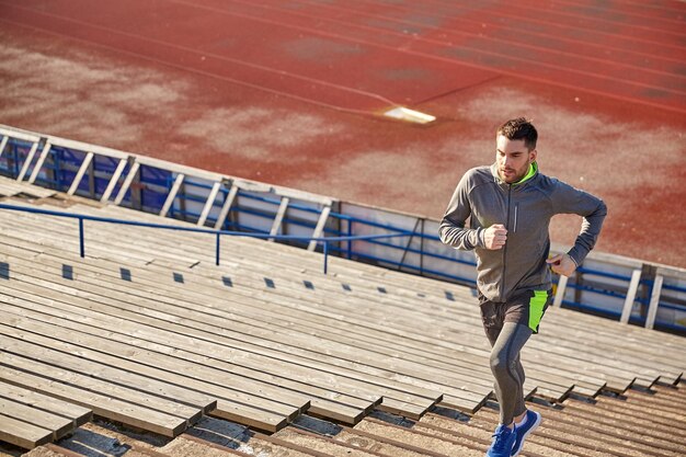 koncepcja fitness, sportu, ćwiczeń i ludzi - młody człowiek biegnący na górę na stadionie