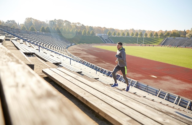 koncepcja fitness, sportu, ćwiczeń i ludzi - szczęśliwy młody człowiek biegnący na górę na stadionie
