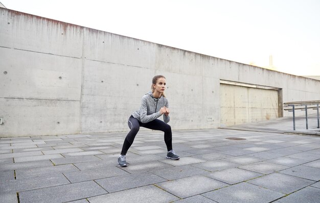 koncepcja fitness, sportu, ćwiczeń i zdrowego stylu życia - szczęśliwa kobieta robi przysiady na świeżym powietrzu