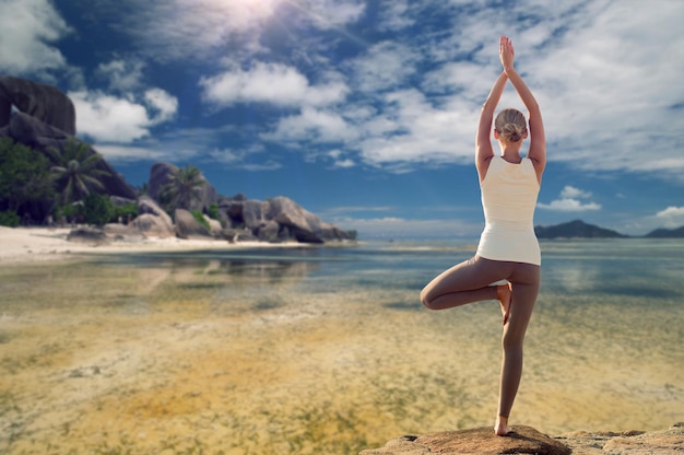 koncepcja fitness, sportu, ludzi i rekreacji - młoda kobieta robiąca pozę drzewa jogi z tyłu na tle egzotycznej tropikalnej plaży