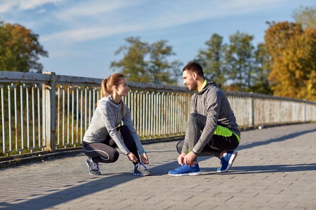 koncepcja fitness, sportu, ludzi i stylu życia - uśmiechnięta para wiązania sznurowadeł na zewnątrz