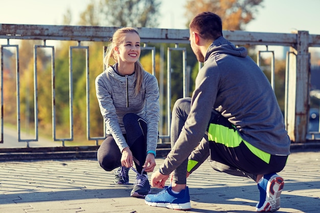 Zdjęcie koncepcja fitness, sportu, ludzi i stylu życia - uśmiechnięta para wiązania sznurowadeł na zewnątrz