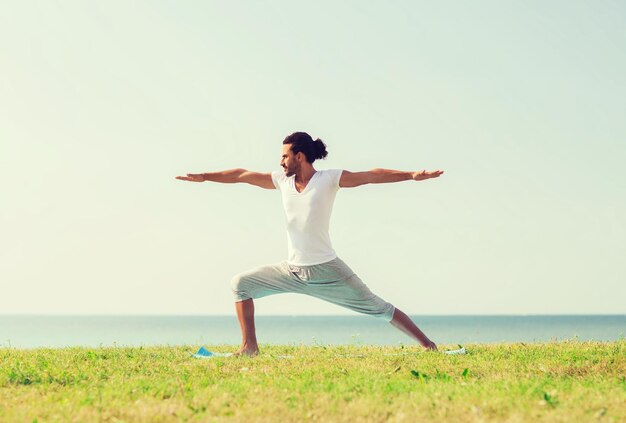 koncepcja fitness, sportu, ludzi i stylu życia - uśmiechnięty mężczyzna wykonujący ćwiczenia jogi na świeżym powietrzu