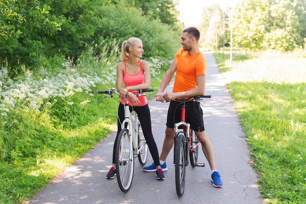 koncepcja fitness, sportu, ludzi i zdrowego stylu życia - szczęśliwa para jeżdżąca na rowerze na świeżym powietrzu latem