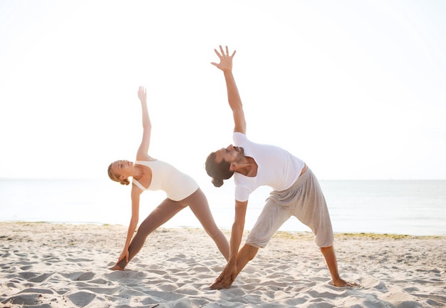 koncepcja fitness, sportu, przyjaźni i stylu życia - para wykonująca ćwiczenia jogi na plaży