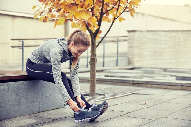 Zdjęcie koncepcja fitness, sportu, przyjaźni i stylu życia - szczęśliwa młoda sportowa kobieta wiąże sznurowadła na zewnątrz