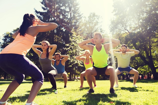 koncepcja fitness, sportu, przyjaźni i zdrowego stylu życia - grupa nastoletnich przyjaciół lub sportowców ćwiczących i wykonujących przysiady na obozie treningowym