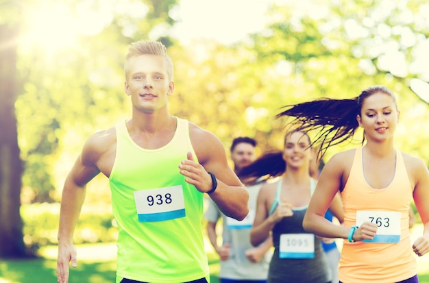 koncepcja fitness, sportu, przyjaźni, rasy i zdrowego stylu życia - grupa szczęśliwych nastoletnich przyjaciół lub sportowców biegających maraton z numerami odznak na zewnątrz