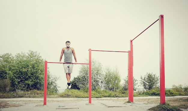 koncepcja fitness, sportu, treningu i stylu życia - młody człowiek ćwiczący na poziomym pasku na zewnątrz