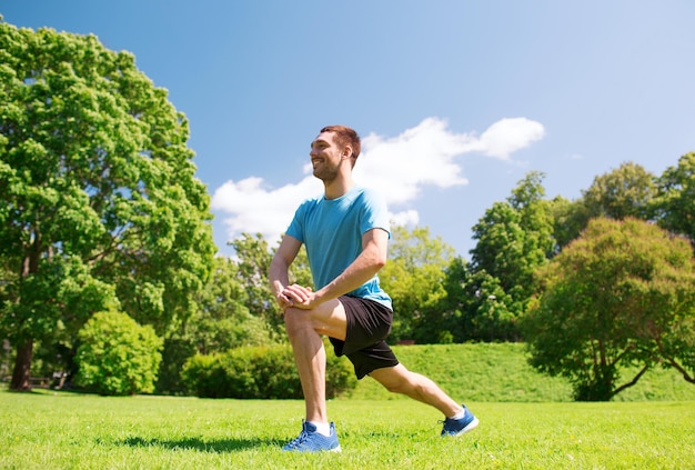 koncepcja fitness, sportu, treningu i stylu życia - uśmiechnięty mężczyzna rozciągający nogę na zewnątrz