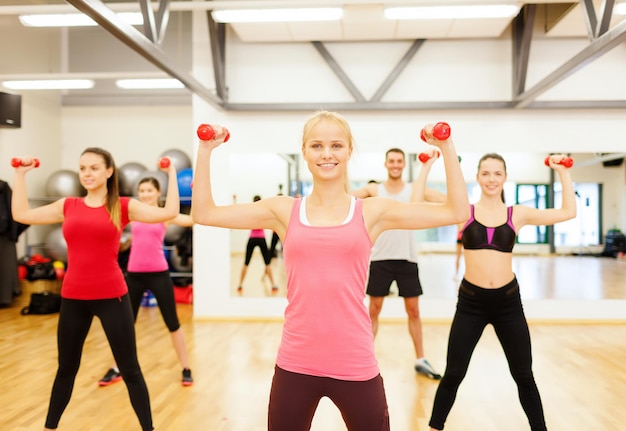 koncepcja fitness, sportu, treningu, siłowni i stylu życia - grupa uśmiechniętych ludzi ćwiczących z hantlami na siłowni