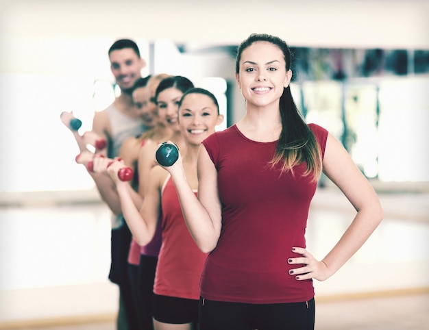 koncepcja fitness, sportu, treningu, siłowni i stylu życia - grupa uśmiechniętych ludzi podnoszących hantle na siłowni