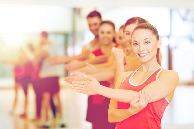 koncepcja fitness, sportu, treningu, siłowni i stylu życia - grupa uśmiechniętych ludzi rozciągających się na siłowni