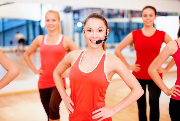 koncepcja fitness, sportu, treningu, siłowni i stylu życia - grupa uśmiechniętych osób z trenerem ćwiczącym na siłowni
