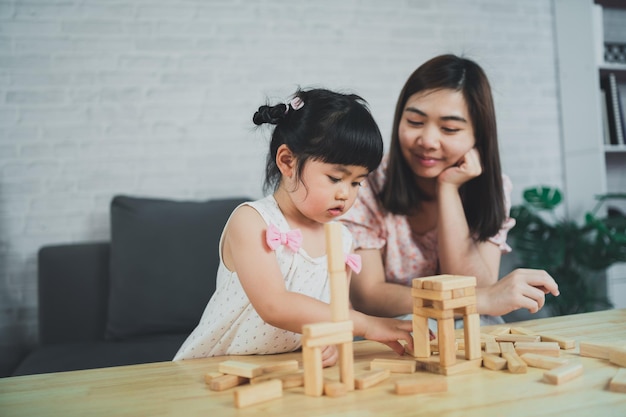 Koncepcja Gier Jenga Azjatycka Córka I Matka Uśmiechają Się Radośnie I śmieją Się Grając W Drewniane Gry Jenga Siedząc Na Kanapie W Salonie W Domu Mama I Córka Rodzinne Zajęcia W Wesołe Gry